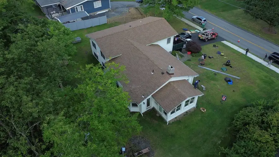 Drone view of a white ranch house with a fresh brown roof, crew gear on the lawn