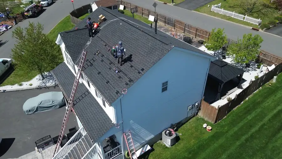 Crew mid tear-off on a blue house, ladders up and the old shingles coming down