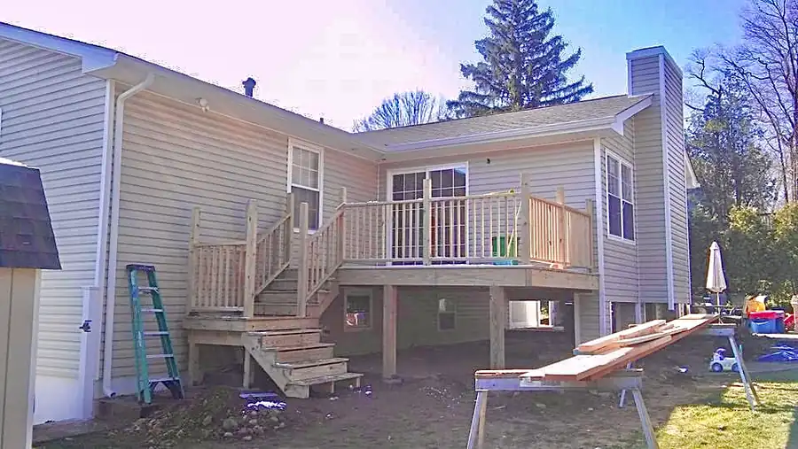 New deck with stairs and railing built out from a vinyl-sided house