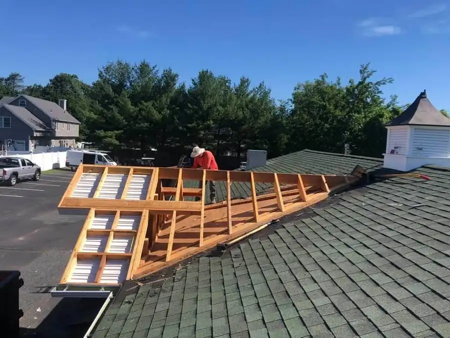 Roof framing opened up beside a cupola, a worker in a red shirt leaning over the rafters