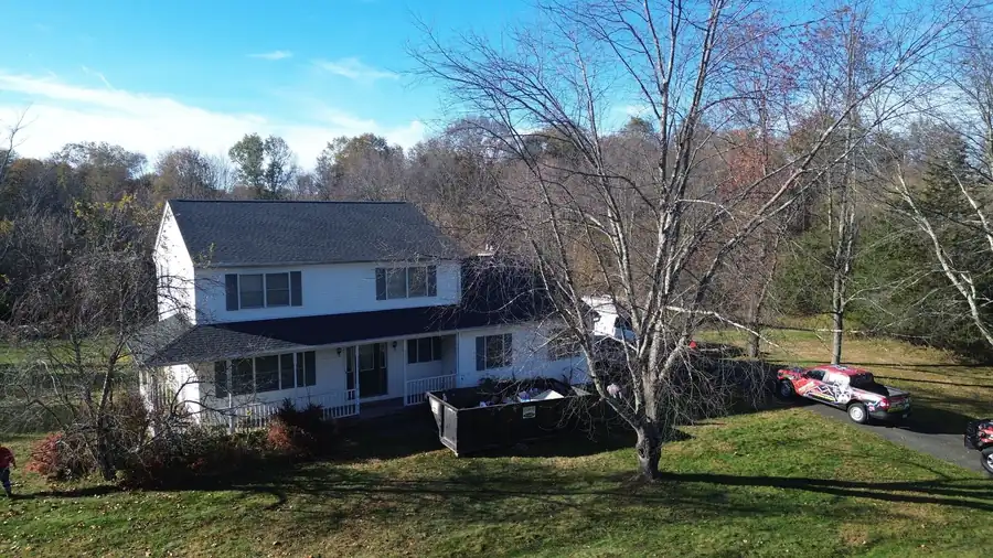 Two-storey house among bare trees with the company truck and a roll-off in the drive