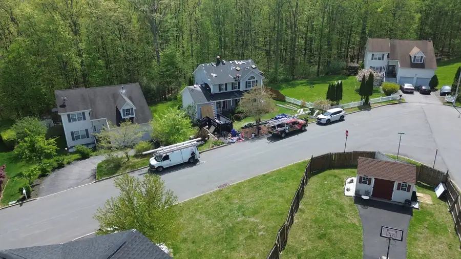Drone view down a wooded cul-de-sac, the crew on a roof and trucks along the street