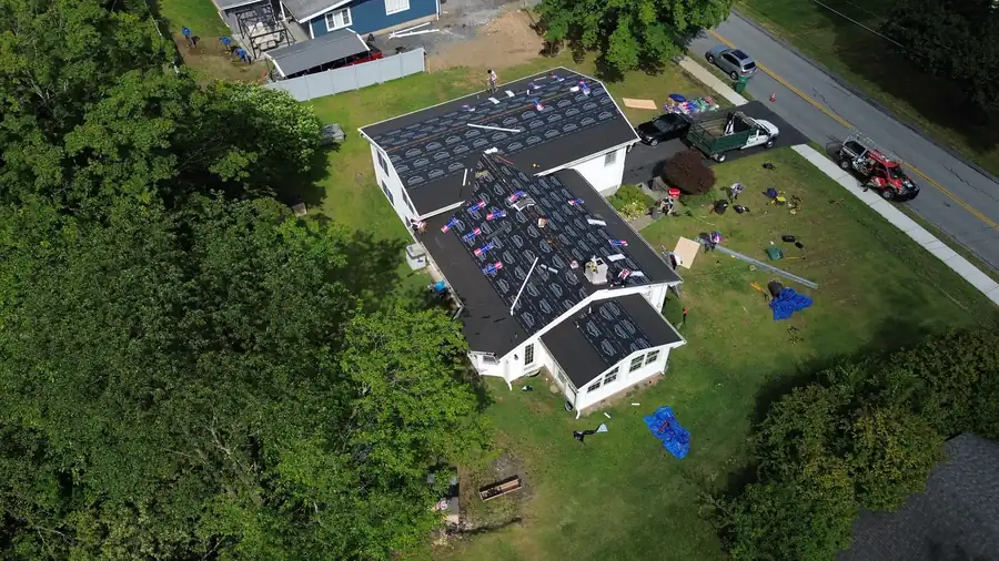 Drone view of a roof stripped to underlayment mid-job, the crew working the ridge